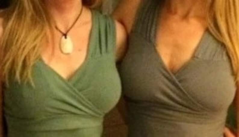 May include: Two women wearing green and gray wrap tops with a deep V-neckline.