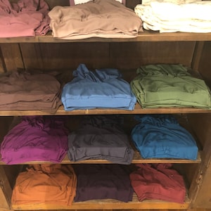 May include: A wooden shelf unit with stacks of folded fabric in various colors, including brown, purple, blue, green, and orange. The fabric is arranged in rows on the shelves.
