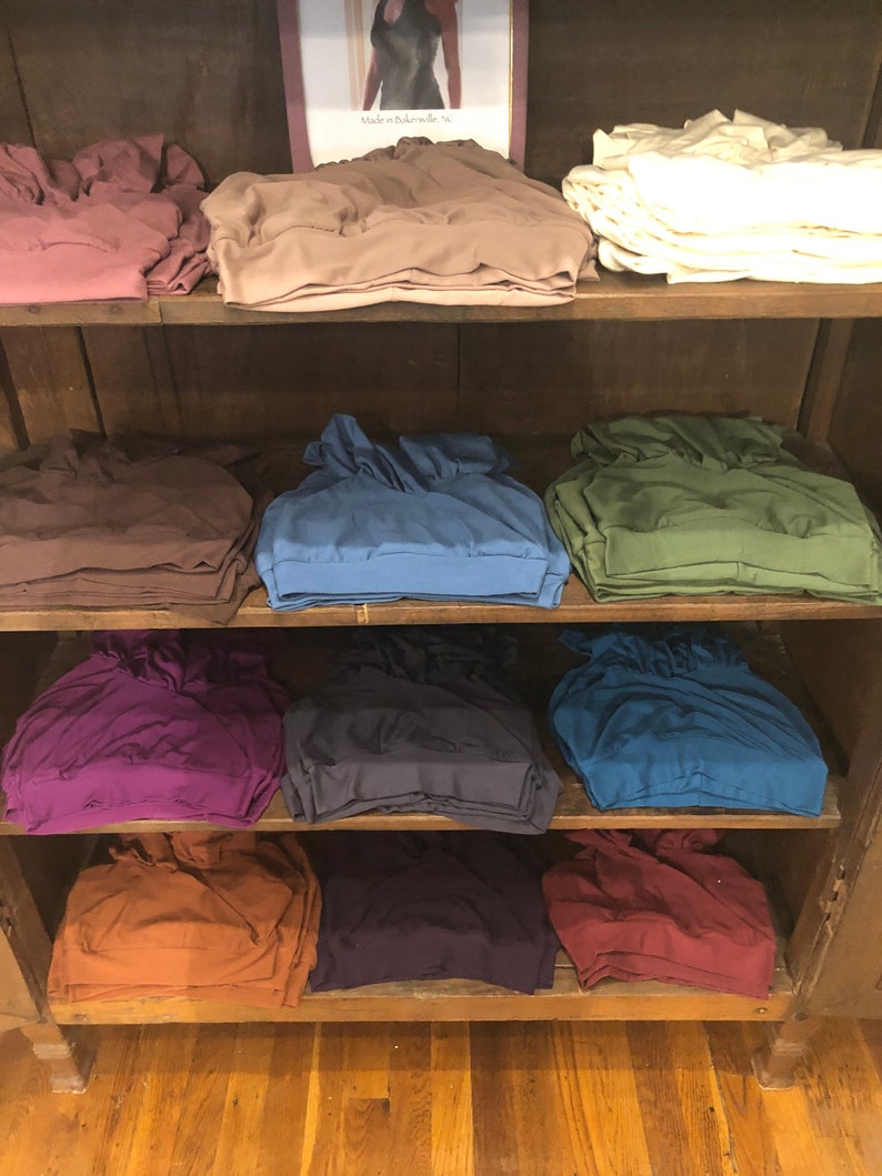 May include: A wooden shelf unit with stacks of folded fabric in various colors, including brown, purple, blue, green, and orange. The fabric is arranged in rows on the shelves.