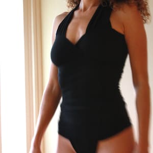 May include: A woman wearing a black halter top with a deep V-neckline. The top is form-fitting and has a smooth texture.