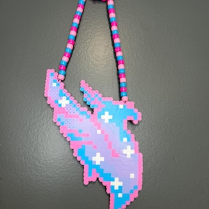 May include: A necklace featuring a pendant made of fused plastic beads in the shape of a stylized bird with wings spread. The pendant is colored in shades of purple, light blue, and pink with white star accents. The chain consists of pink and blue beads.
