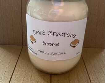 Könnte beinhalten: Eine Kerze im durchsichtigen Glas mit silbernem Metalldeckel und cremefarbenem Wachs. Das weiße Etikett trägt den Text 'funkE Creations', 'Smores' und '100% Soy Wax Candle' sowie Illustrationen von S'mores auf beiden Seiten des Namens.