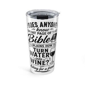Op de afbeelding: Een witte roestvrijstalen beker met een doorzichtig plastic deksel en zwarte tekst: DOES ANYONE know WHAT PAGE OF THE Bible EXPLAINS HOW TO TURN WATER into WINE? Asking for a friend! Het ontwerp bevat kleine iconen van een bijbel en een wijnglas.