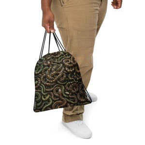 May include: A drawstring bag featuring a detailed, repeating pattern of intertwined snakes in shades of brown, green, and black. The bag has black cord straps and a soft, flexible fabric construction, designed for carrying items with a secure closure.