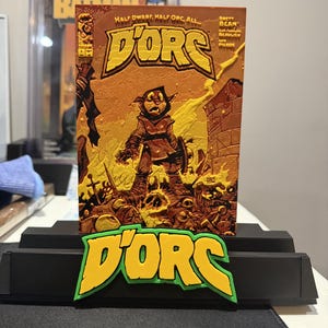 May include: A D'ORC comic book cover featuring a hooded character standing amidst a battlefield of skulls and debris, with the title text "HALF DWARF, HALF ORC, ALL... D'ORC" printed above. A matching yellow and green D'ORC logo sits on a black stand.