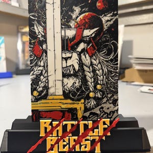 May include: A rectangular display plaque featuring a graphic illustration of a lion warrior with a sword, set against a black background with red planets. The base is black with the yellow text BATTLE BEAST overlaid by three red claw marks.