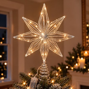 Peut inclure: Une étoile décorative argentée à plusieurs branches pour sommet de sapin, dotée d'une structure en fil métallique et de lumières LED blanc chaud intégrées. L'étoile est fixée sur une base en spirale métallique avec un petit boîtier à piles.