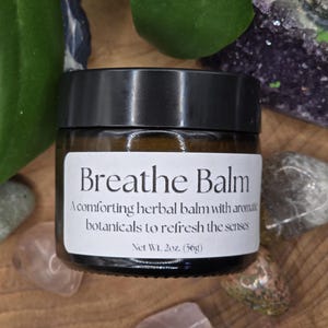 May include: A small amber glass jar with a black lid containing Breathe Balm. The white label features the text: Breathe Balm, A comforting herbal balm with aromatic botanicals to refresh the senses, Net Wt. 2oz. (56g).