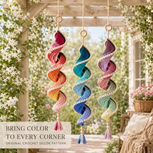 May include: Three hanging spiral crochet decorations suspended by wooden rings. The left spiral features a warm gradient from deep red to yellow. The center spiral transitions from dark blue to light blue. The right spiral displays a cool purple to green gradient.
