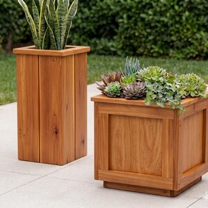 Könnte beinhalten: Zwei Pflanzgefäße aus Holz mit natürlichem Finish. Eines ist ein hohes, rechteckiges vertikales Pflanzgefäß mit einer Bogenhanf-Pflanze. Das andere ist ein kürzeres, quadratisches Pflanzgefäß mit verschiedenen grünen und violetten Sukkulenten.
