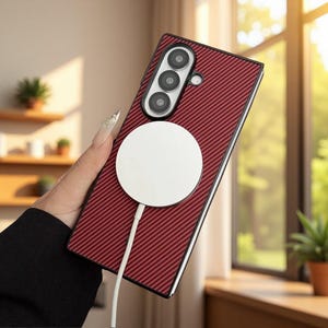 May include: A rectangular smartphone case with a dark red carbon fiber texture. The case features a vertical camera array with three lenses and a circular white magnetic wireless charging puck attached to the center with a white power cable.