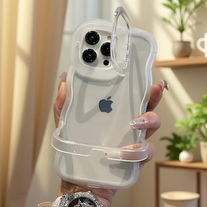 Puede incluir: Una funda de teléfono transparente con bordes ondulados para iPhone con sistema de triple cámara. La funda cuenta con una cubierta circular articulada integrada única que se abre para proteger las lentes, con un diseño elegante y claro.