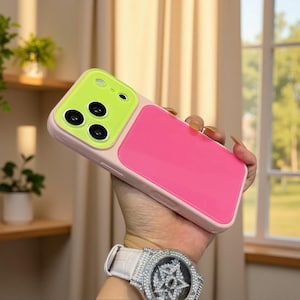 Könnte beinhalten: Eine Smartphone-Hülle mit einem leuchtend neongrünen Kameramodulbereich mit drei kreisförmigen Aussparungen für die Linsen und einer großen, glatten, kräftig pinkfarbenen rechteckigen Platte auf der Rückseite, eingefasst in einen blassrosa Rahmen.