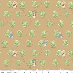 May include: A tan fabric featuring a repeating pattern of light green lettuce heads and small brown rabbits in various poses, including some wearing blue jackets. A white ruler measuring 12 inches is visible along the bottom edge of the image.