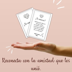 Può includere: Due carte rettangolari bianche con testo nero e un'illustrazione a cuore, che riportano il titolo AQUÍ ENTRE DOS e la domanda ¿Te conozco? insieme a istruzioni. Sotto ci sono tre icone etichettate Descarga, Imprime e Reconecta.