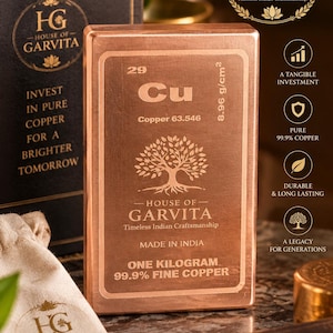 May include: A rectangular copper bar weighing one kilogram, featuring the periodic table symbol Cu, atomic number 29, and the House of Garvita logo. The surface displays a tree emblem, the text 99.9% Fine Copper, and Made in India, presented with a branded pouch.
