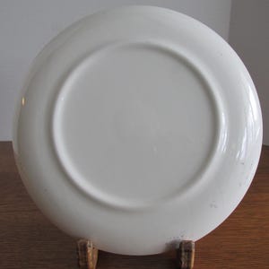 May include: White ceramic plate with a slightly raised rim. The plate is plain white with no design or pattern.