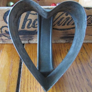 May include: A vintage metal heart-shaped cookie cutter. The cutter is made of a dark gray metal and has a smooth, slightly worn surface.