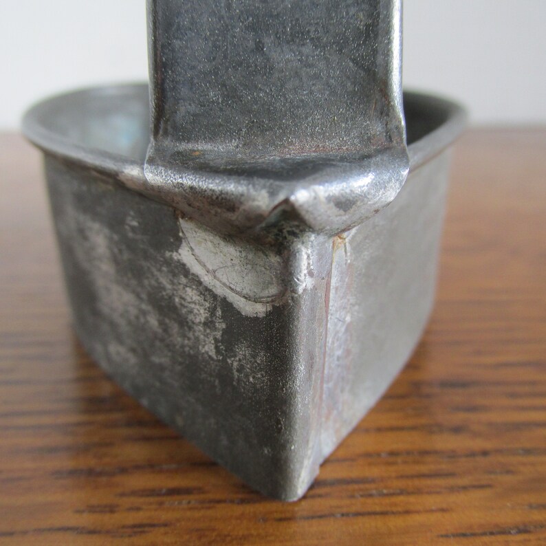 May include: A vintage metal heart-shaped cookie cutter with a handle. The cutter has a worn, silver finish with some rust spots.