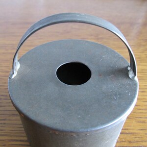 May include: A vintage metal cake pan with a handle. The pan is round and has a hole in the center. It is a dark gray color and shows signs of wear.
