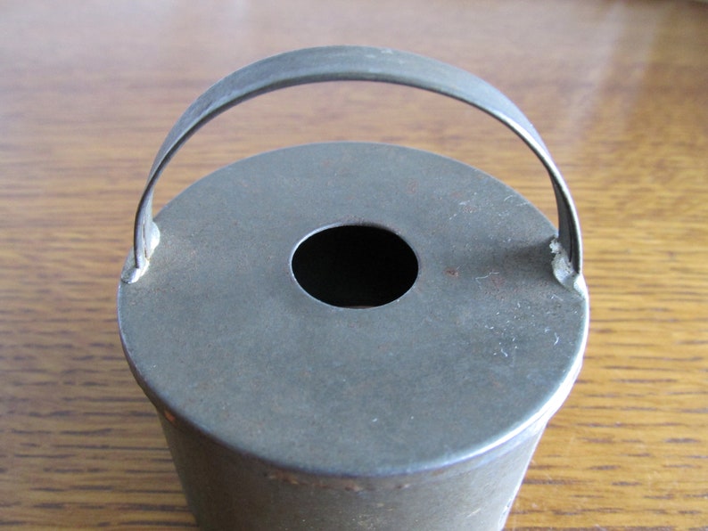 May include: A vintage metal cake pan with a handle. The pan is round and has a hole in the center. It is a dark gray color and shows signs of wear.