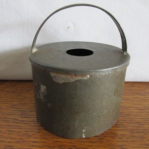May include: A vintage metal cookie cutter in the shape of a bucket with a handle. The cutter is green and has a hole in the top.