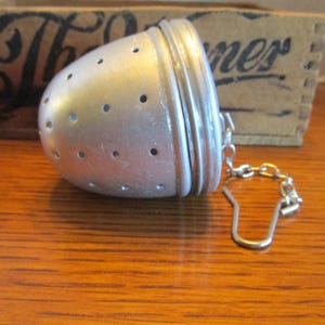 May include: Silver tea infuser with a chain and hook. The infuser has a round, bulbous shape with small holes for steeping tea.