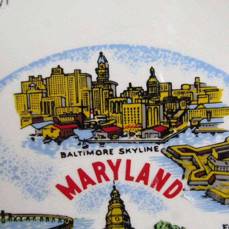 May include: A white ceramic plate with a colorful illustration of the Baltimore skyline, including the Inner Harbor and Fort McHenry. The text "Baltimore Skyline" and "Maryland" is printed in red and black.