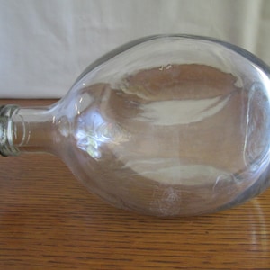 May include: A clear glass bottle with a round body and a long neck. The bottle has a white plastic cap.