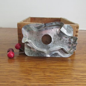 May include: Vintage metal cookie cutter shaped like a bird. The cutter is silver with a worn, rustic look.