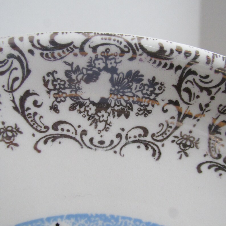 May include: Close-up of a white ceramic plate with a black and gold floral pattern around the edge.