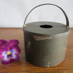 May include: A vintage metal cake mold with a handle. The mold is green and has a circular shape with a hole in the center. The mold is sitting on a wooden surface.