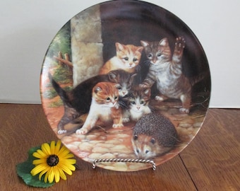 May include: Decorative plate featuring a charming scene of playful kittens and a hedgehog. The plate showcases a detailed illustration with warm colors, depicting the animals in a natural setting. A yellow flower adds a touch of color.