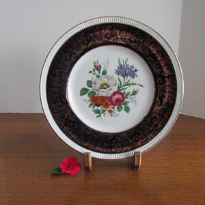 May include: A white porcelain dinner plate with a gold and blue rim and a floral design in the center. The flowers are white, red, orange, and blue.
