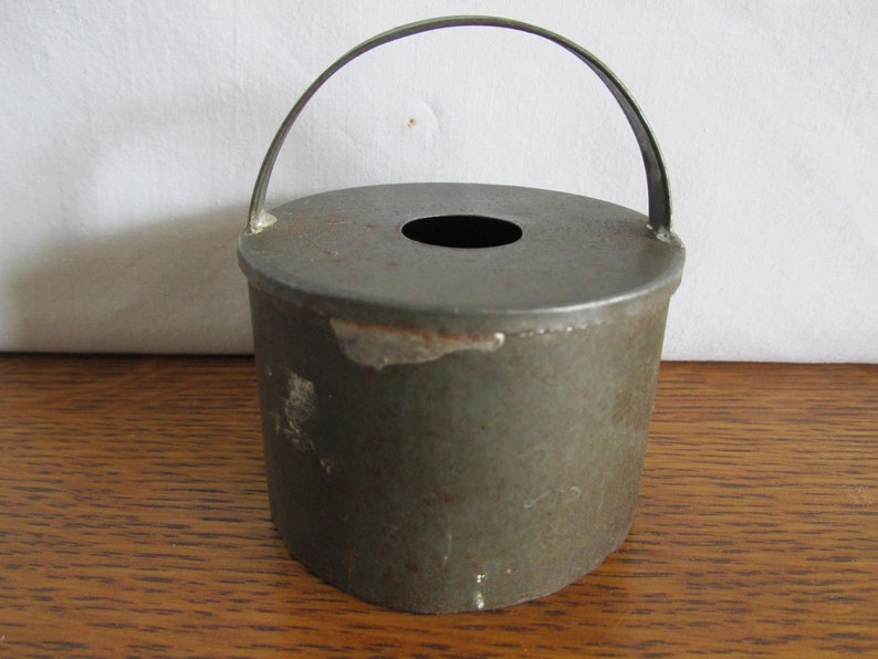 May include: A vintage metal cookie cutter in the shape of a bucket with a handle. The cutter is green and has a hole in the top.
