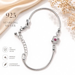 Puede incluir: Una pulsera de plata de ley 925 con una cadena delicada, un cierre de mosquetón y un dije hexagonal central con una pequeña piedra roja ovalada rodeada de diminutas piedras claras. El texto 925 STARLING SILVER es visible.