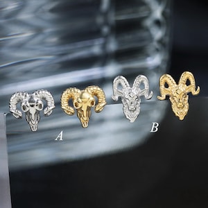 May include: Four ram skull stud earrings arranged in a row. The first and third are silver-toned, while the second and fourth are gold-toned. The second earring is labeled with the letter A, and the fourth earring is labeled with the letter B.