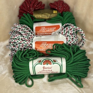 May include: A stack of four bundles of braided macrame cord. The top bundle is red with silver flecks, two middle bundles are white with red and green flecks labeled EZKNOT, and the bottom bundle is solid green labeled Darice Braided Macrame Cord.