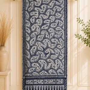 Könnte beinhalten: Ein rechteckiger Wandbehang aus Textil mit einem dunkelblau-weißen Batikmuster. Das Mittelfeld zeigt ein dichtes, sich wiederholendes blattartiges Motiv, eingerahmt von einer dunkelblauen Bordüre mit einem weißen farnartigen Design.