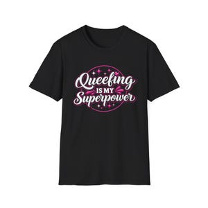 May include: A black short-sleeved t-shirt featuring a circular graphic design in pink and white. The text reads "Queefing IS MY Superpower" in a stylized script font, surrounded by small pink star and heart accents centered on the chest.
