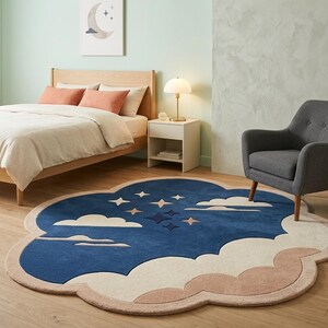 May include: A cloud-shaped area rug featuring a deep blue center with a pattern of white and light pink stars and clouds. The rug has a thick, light pink border that follows the scalloped, rounded edges of the cloud-like design.