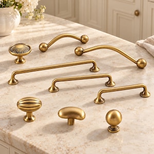 May include: A collection of brass-toned cabinet hardware including three arched pulls, three straight bar pulls, and four knobs in various shapes such as round, oval, and ribbed designs. The hardware features a smooth, metallic finish.