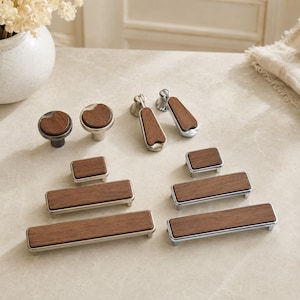 May include: A collection of cabinet hardware including two round knobs, two drop pulls, and four rectangular drawer pulls. Each piece features a dark brown wood inlay set into a metallic base with a smooth, polished silver or dark grey finish.