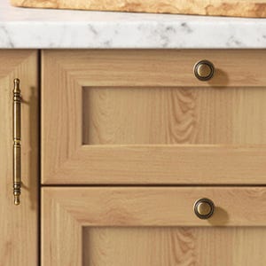 May include: A set of light wood kitchen cabinets featuring a long, vertical antique brass handle on the left door and two round, matching antique brass knobs on the right-hand drawers, all set against a light wood grain cabinet surface.