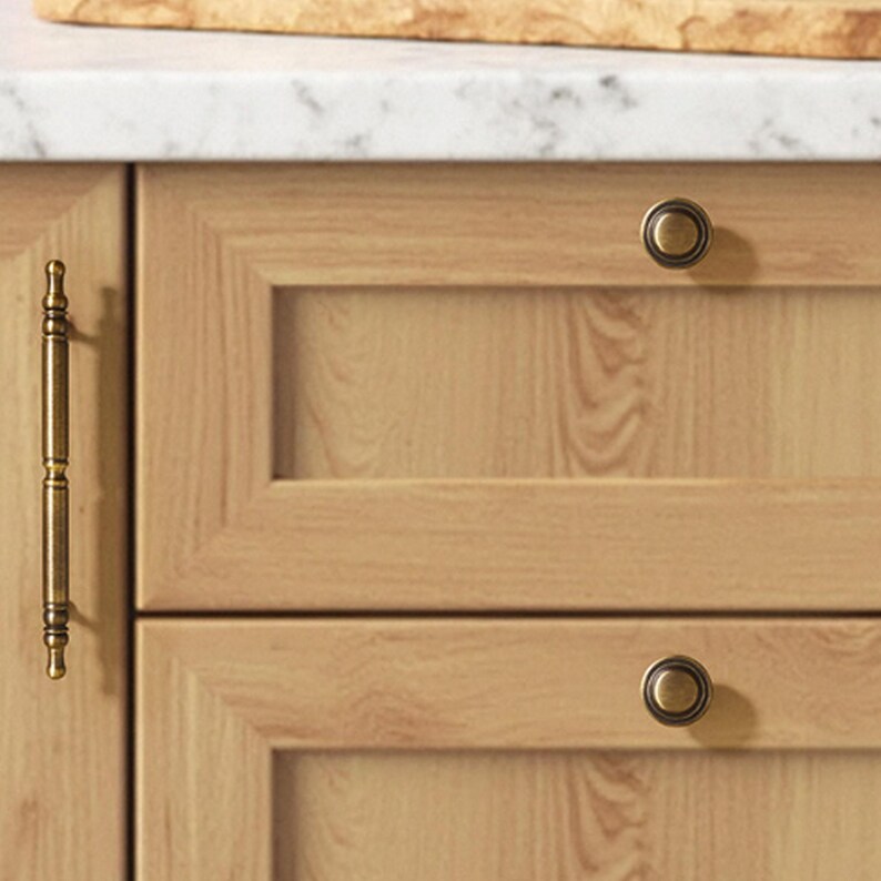 May include: A set of light wood kitchen cabinets featuring a long, vertical antique brass handle on the left door and two round, matching antique brass knobs on the right-hand drawers, all set against a light wood grain cabinet surface.
