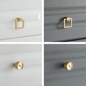 May include: A collection of four gold-toned metal cabinet knobs and pulls. Two feature a square drop-ring design, while the other two are shaped like circular buttons with four central holes, all mounted on white or dark gray drawer fronts.