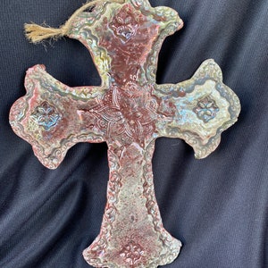 May include: A ceramic cross with a white and brown glaze. The cross has a detailed design with a floral pattern.