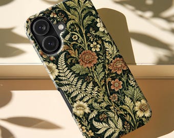 Könnte beinhalten: Eine Smartphone-Hülle mit dunkelgrünem Hintergrund und einem dichten botanischen Muster aus cremefarbenen Farnen, gedeckten orangefarbenen Blüten und hellgrünem Blattwerk. Die Hülle hat eine Aussparung für eine Doppelkamera und einen Blitz oben links.