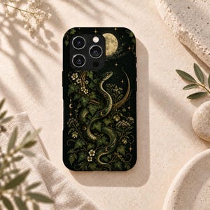 May include: A black smartphone case featuring a detailed illustration of a green snake coiled among ivy leaves and white flowers. The design includes a full moon, small stars, and crescent moon symbols against a dark background with a triple camera lens.