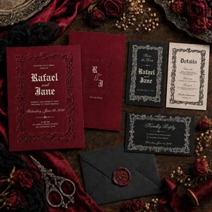 May include: A wedding stationery set featuring deep red and black cards with ornate, raised-texture frames. The text includes names Rafael and Jane, date June 22, 2026, and details. Includes a black envelope with a red wax seal and metal scissors.